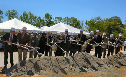 A group of Johnston Hospital Foundation campaign leaders wearing white hard hats hold shovels as they break ground